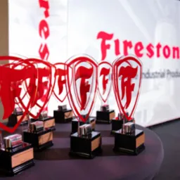 Szereg nagród z logo firmy Firestone, ustawionych na stole podczas uroczystości firmowej.