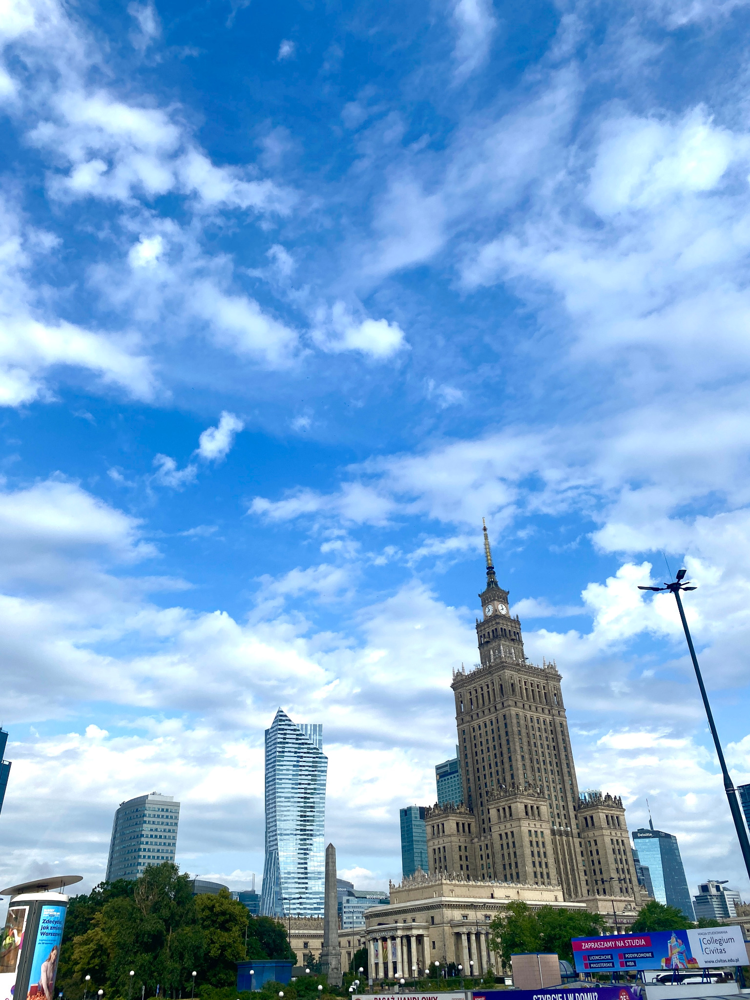 Panorama Warszawy z Pałacem Kultury i Nauki oraz nowoczesnymi wieżowcami na tle błękitnego nieba z chmurami, widok z dołu.