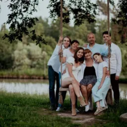 Rodzinne zdjęcie grupowe na huśtawce zawieszonej na drzewie, w tle zielony krajobraz i staw.