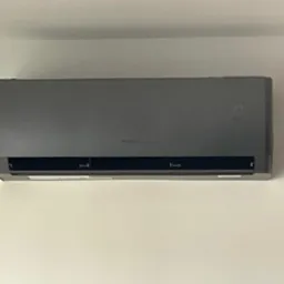 Szara jednostka wewnętrzna klimatyzacji marki Gree zamontowana na białej ścianie, wyświetlająca temperaturę 20 stopni Celsjusza.