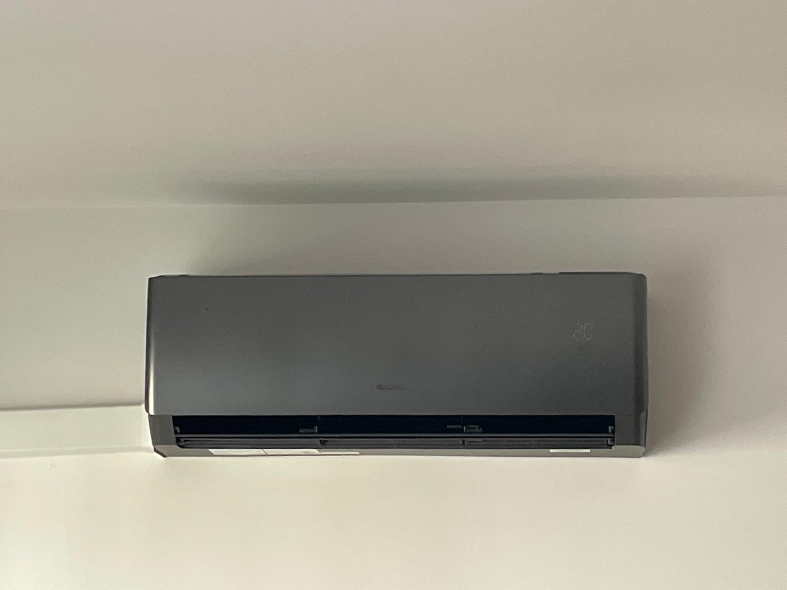 Nowoczesny, grafitowy klimatyzator marki Gree zamontowany na białej ścianie, wyświetlający temperaturę 26 stopni Celsjusza.