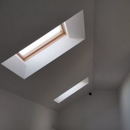 Mar-Dom Marek Adamczyk - Poddasze z dwoma oknami dachowymi o drewnianych ramach i białych wnękach, świeżo pomalowane na biało, widoczne przewody i rury przy podłodze.