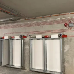 Instalacja przeciwpożarowa z licznymi przewodami i czujnikami zamontowana na surowej ścianie w budynku we Wrocławiu.