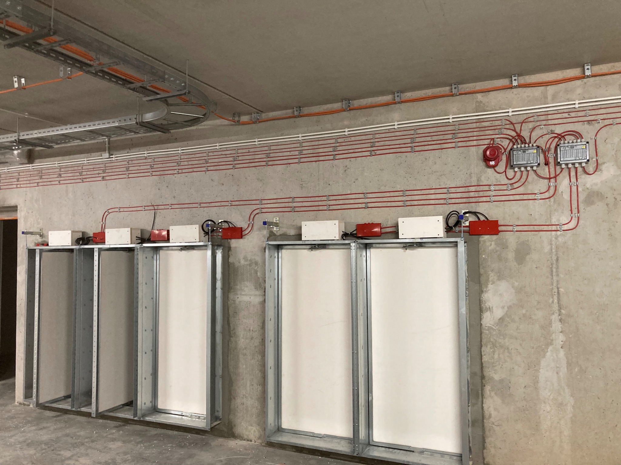 Instalacja przeciwpożarowa z licznymi przewodami i czujnikami zamontowana na surowej ścianie w budynku we Wrocławiu.