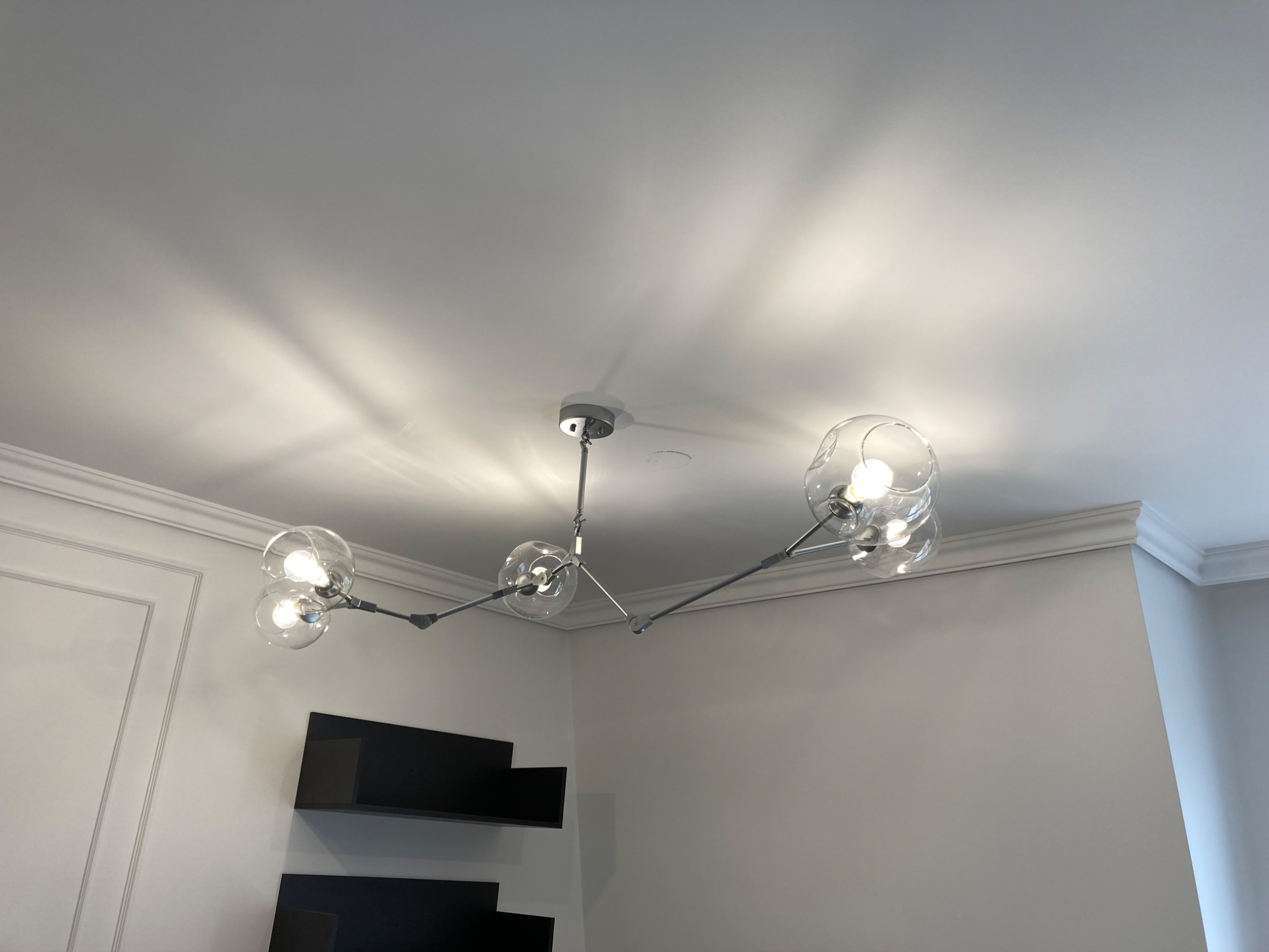 Nowoczesny żyrandol z przezroczystymi kulami zawieszony na suficie, oświetlający białe ściany i czarne półki
