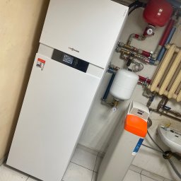 Hydro Tech - Kompaktowy, biały piec grzewczy Viessmann z widocznym wyświetlaczem, obok biały filtr wody Viteco z pomarańczową górną częścią, czerwony zbiornik wyrównawczy i fragment grzejnika żeberkowego w tle.