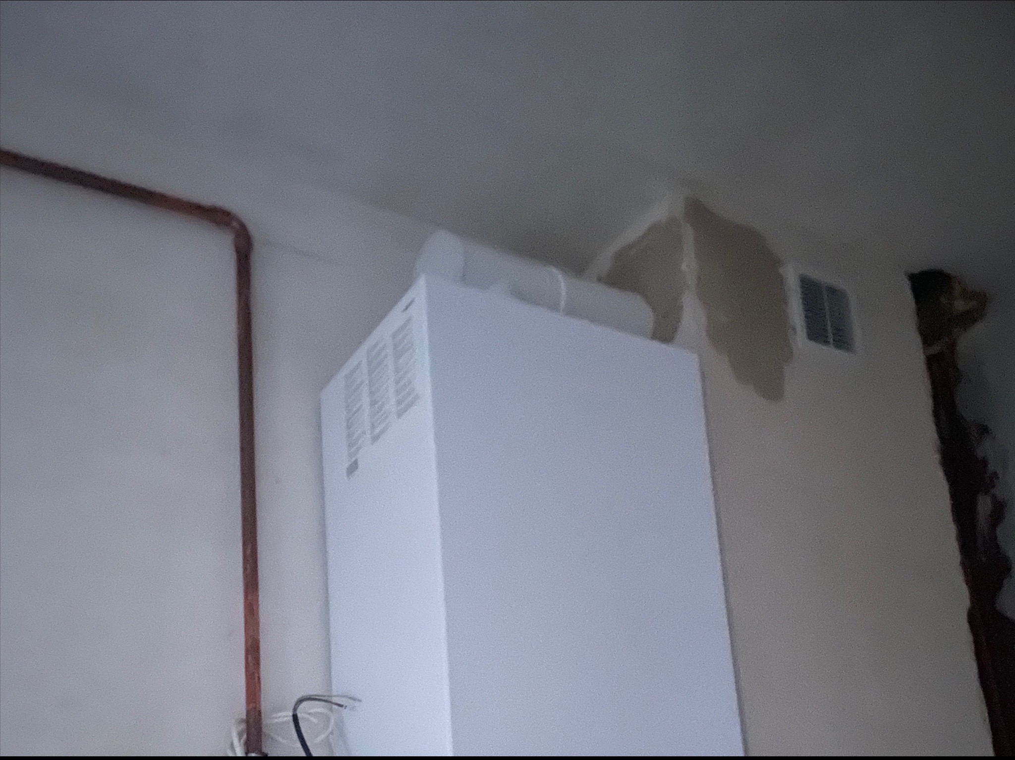 Biały piec grzewczy z podłączeniami wentylacyjnymi i miedzianą rurą instalacji w Pyskowicach, widoczne ślady po pracach remontowych na ścianie.