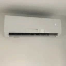 Biały klimatyzator ścienny marki Sinclair w minimalistycznym wnętrzu, wyświetlający temperaturę 18 stopni Celsjusza.