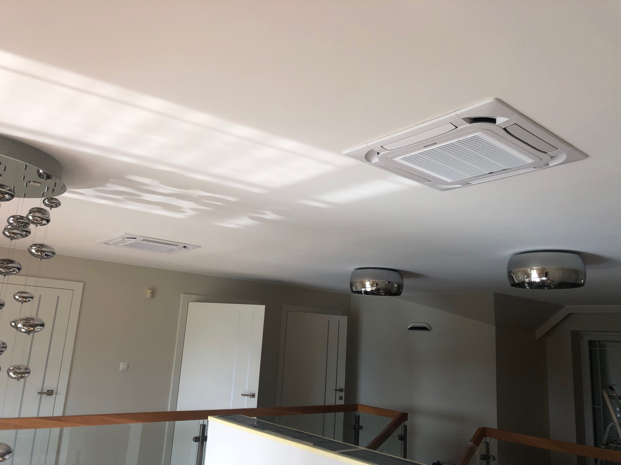 Kasetonowa jednostka klimatyzacyjna wmontowana w sufit podwieszany, widok z poziomu antresoli z balustradą, nowoczesne oświetlenie sufitowe.