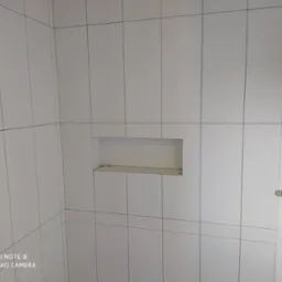 Ściana łazienki wyłożona białymi, matowymi płytkami ceramicznymi z wąską fugą, wnęka w ścianie z półką i przygotowane miejsce na baterię.