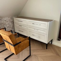BDM Furniture - Biała komoda z sześcioma szufladami na czarnych nóżkach, z drewnianym blatem, stojąca w pokoju na poddaszu, obok dwa pomarańczowe fotele z czarną ramą, podłoga ułożona w jodełkę.