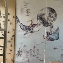 Pokój dziecięcy z tapetą w motywy morskie i balony, ścianka wspinaczkowa z drewnianymi panelami i uchwytami, huśtawka linowa, parkiet w jodełkę.