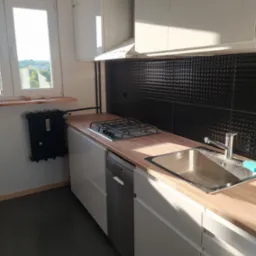 Nowoczesna kuchnia z białymi szafkami, bukowym blatem, czarną, wypukłą mozaiką na ścianie, widokiem z okna i starodawnym grzejnikiem żeliwnym.