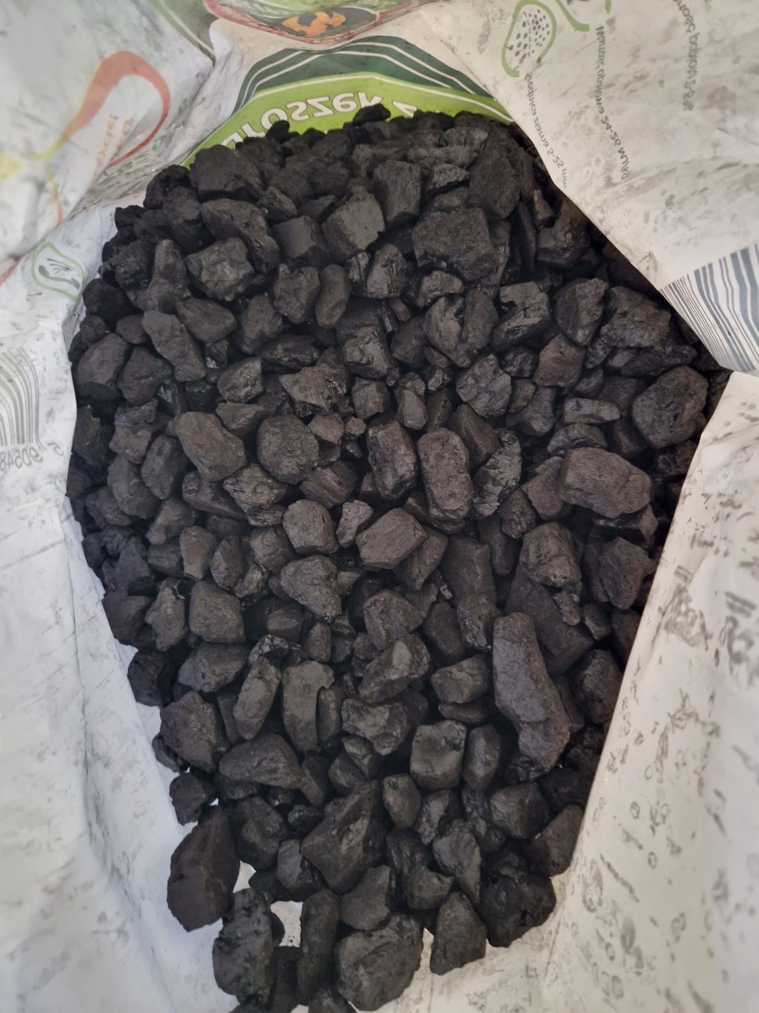 Wnętrze worka wypełnionego czarnymi bryłkami opału, widoczne fragmenty nadruku na worku.