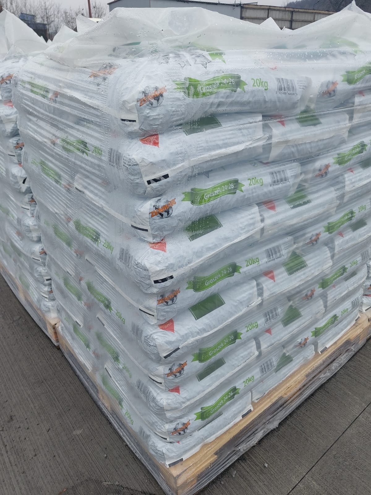Paleta z workami 20kg z napisem 'Eko Groszek 24-26', owinięta folią, na zewnątrz, widoczne drzewa w tle.