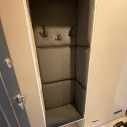 Wnęka w zabudowie meblowej z tapicerowanym siedziskiem i ścianami w szarym kolorze, wyposażona w trzy wieszaki na ubrania.