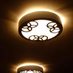 Dwa okrągłe plafony LED z ażurowym wzorem w kształcie czterolistnych kwiatów, o ciepłej barwie światła, zamontowane na ciemnym suficie. Widoczny czujnik dymu w tle.