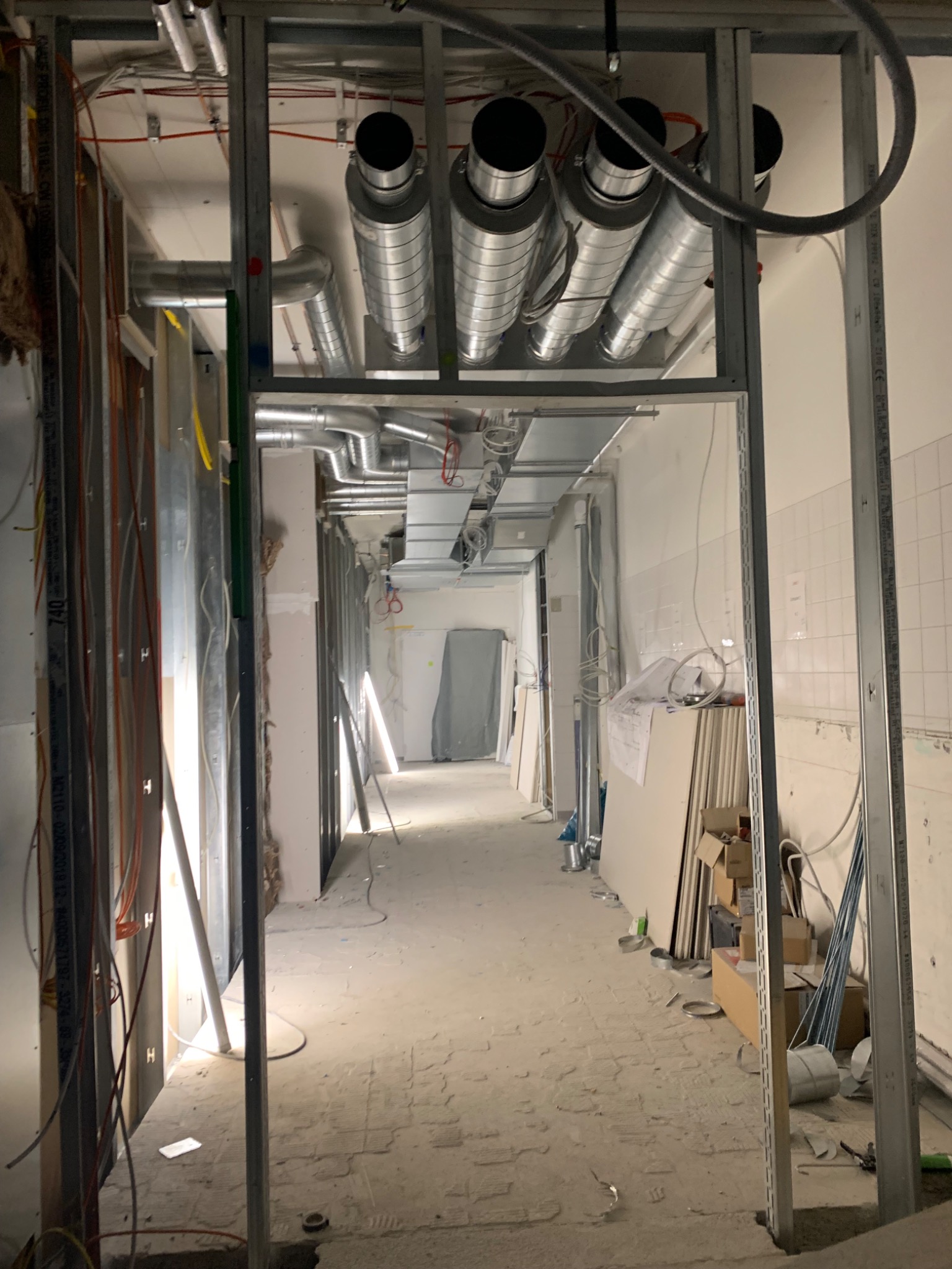 Wnętrze w trakcie remontu z widocznymi elementami instalacji wentylacyjnej pod sufitem, metalowymi profilami ścianek działowych i przewodami elektrycznymi.