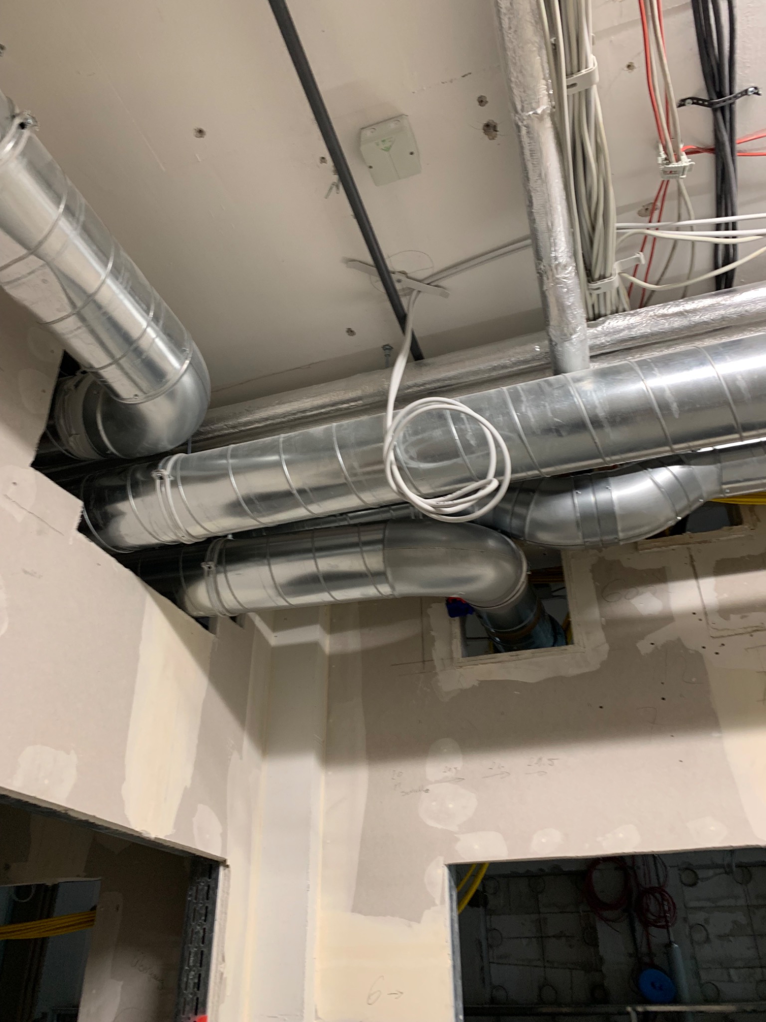 Montaż systemu wentylacji mechanicznej z rurami spiro na suficie w budynku w stanie deweloperskim, widoczne kable i instalacje elektryczne.