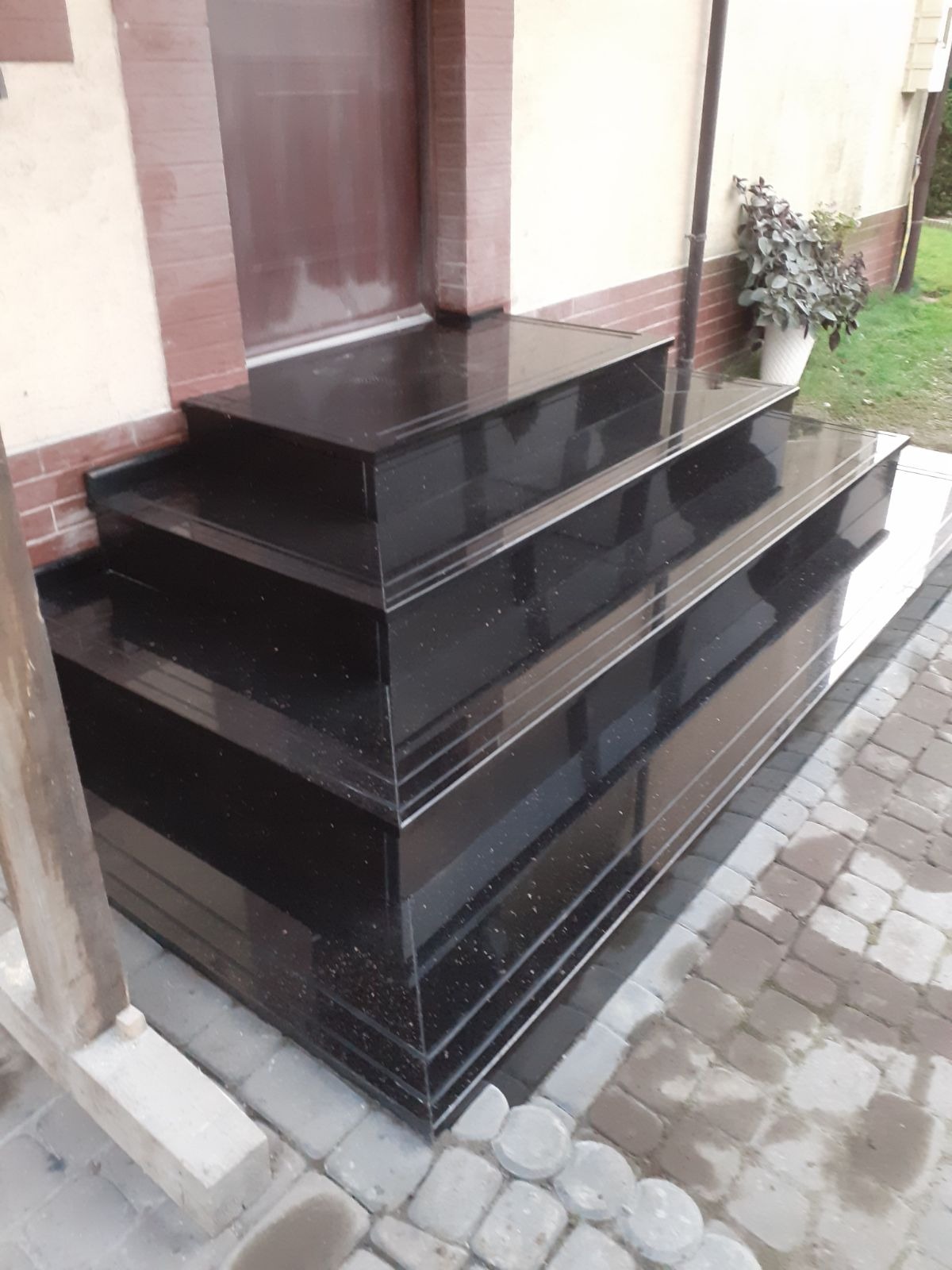 Zewnętrzne, trzy-stopniowe schody wejściowe wykonane z czarnego, błyszczącego kamienia z drobinkami, prowadzące do drzwi wejściowych domu.