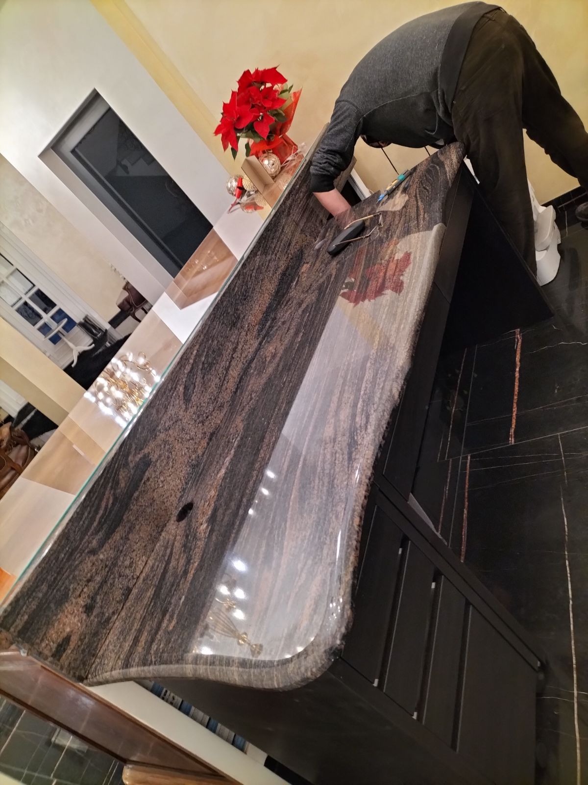 Montaż blatu z ciemnego, wzorzystego kamienia w kuchni, widoczny pracownik w trakcie pracy, w tle bożonarodzeniowa dekoracja.