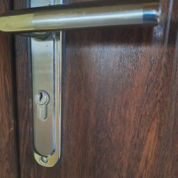 Ślusarz Awaryjne otwieranie aut mieszkań zamków - Zamek drzwiowy z klamką na ciemnych, drewnianych drzwiach, widoczny z bliska.