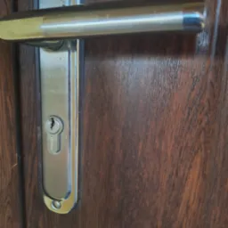 Zamek drzwiowy z klamką na ciemnych, drewnianych drzwiach, widoczny z bliska.