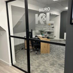K&L profesjonalne czyszczenie - Szklane drzwi z napisem 'BIURO K&L PROFESJONALNE CZYSZCZENIA', widok na biuro z biurkiem, krzesłem i regałem.