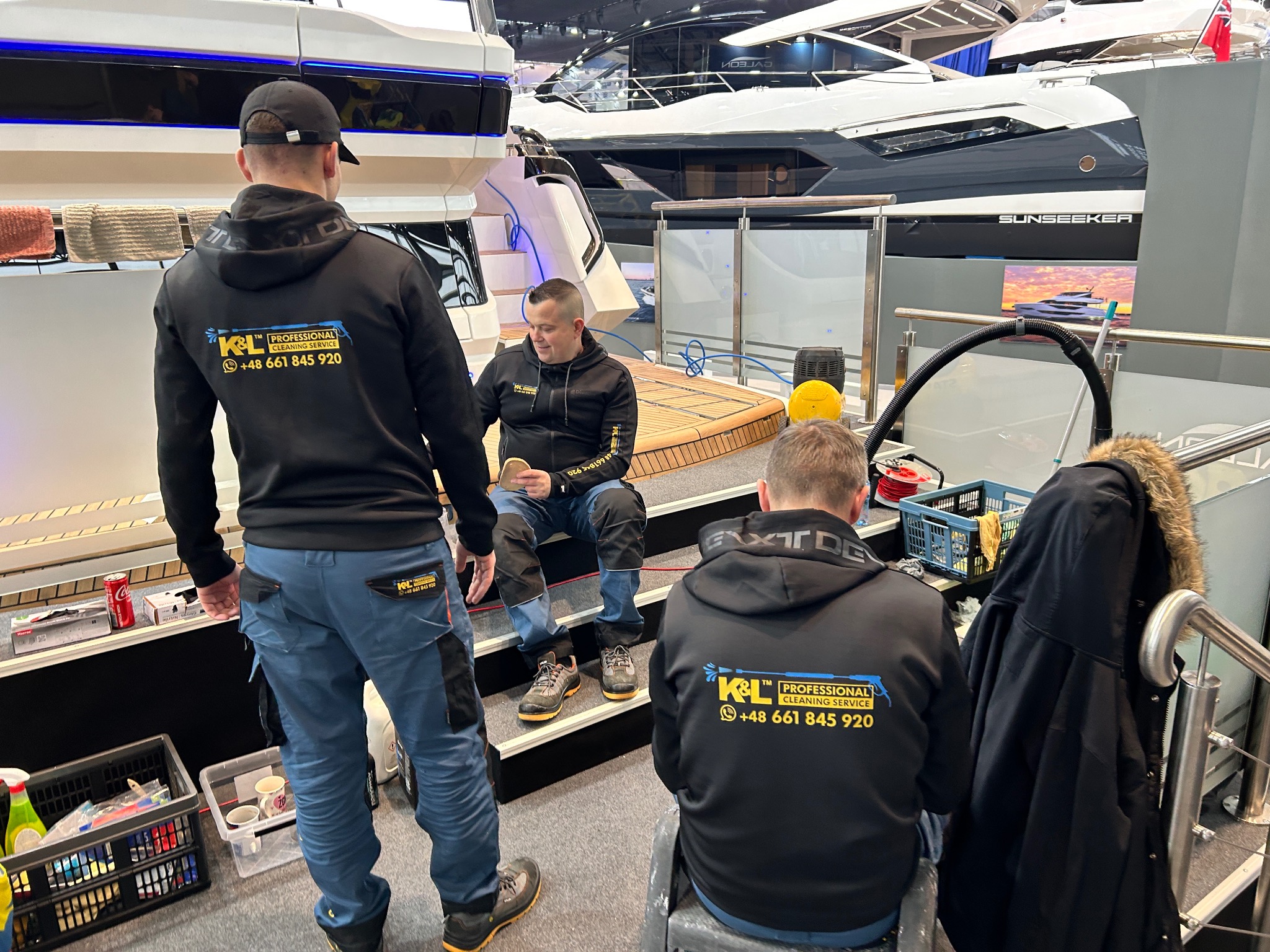 Ekipa sprzątająca w Kwidzynie podczas czyszczenia luksusowego jachtu na targach, widoczne środki czystości i pracownicy w uniformach z logo firmy.