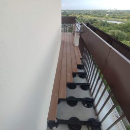 Yolo Bartosz Antonik - Montaż desek kompozytowych na balkonie z widocznymi elementami konstrukcyjnymi i panoramą miasta w tle.
