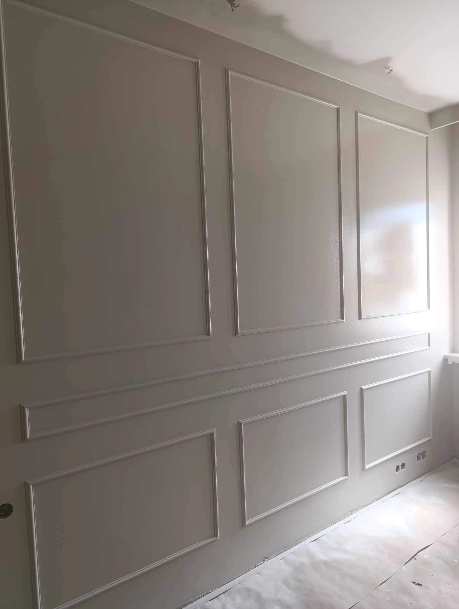 Ściana w kolorze złamanej bieli z dekoracyjnymi listwami tworzącymi prostokątne panele, zabezpieczona folią podłoga.