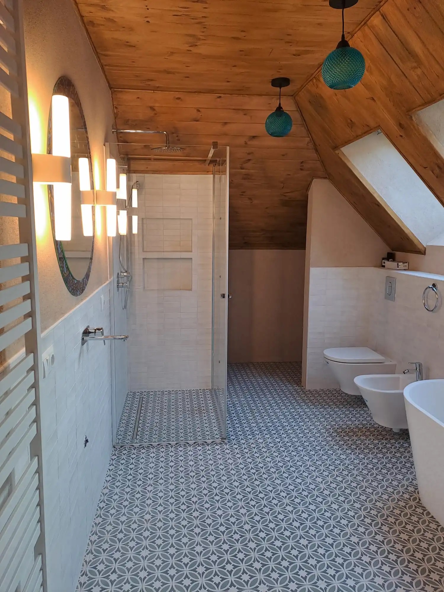 Nowoczesna łazienka na poddaszu z drewnianym sufitem, kabiną prysznicową typu walk-in, umywalką, bidetem i toaletą, oświetlona designerskimi lampami w kształcie kuli.