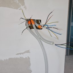 Usługi Inżynierskie mgr inż. Monika Wójcicka - Instalacja elektryczna w trakcie montażu w ścianie w Czańcu, widoczne kable w peszlach i puszka instalacyjna.