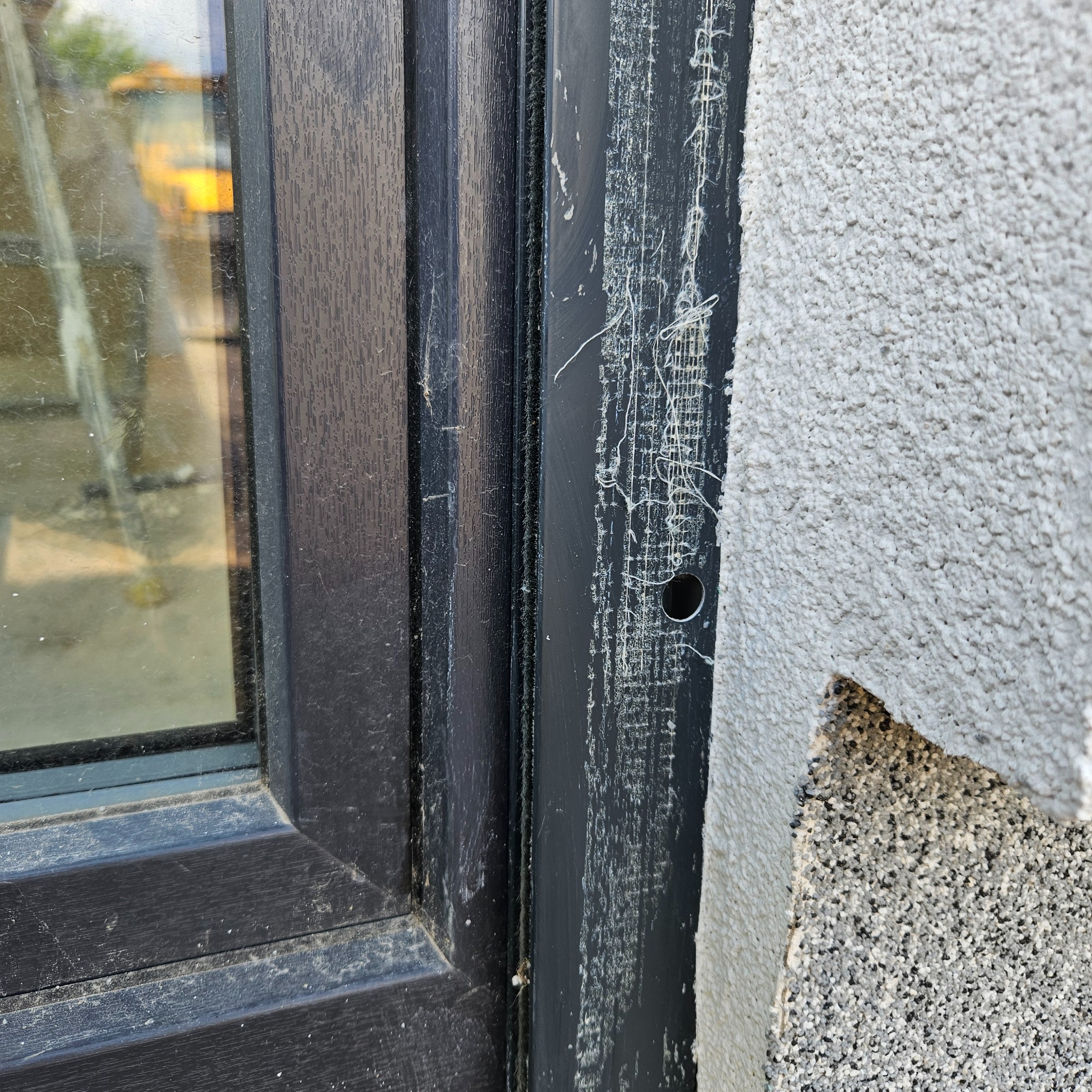 Fragment elewacji z oknem w trakcie prac wykończeniowych: widoczne ślady po taśmie malarskiej, resztki kleju i otwór w elewacji.