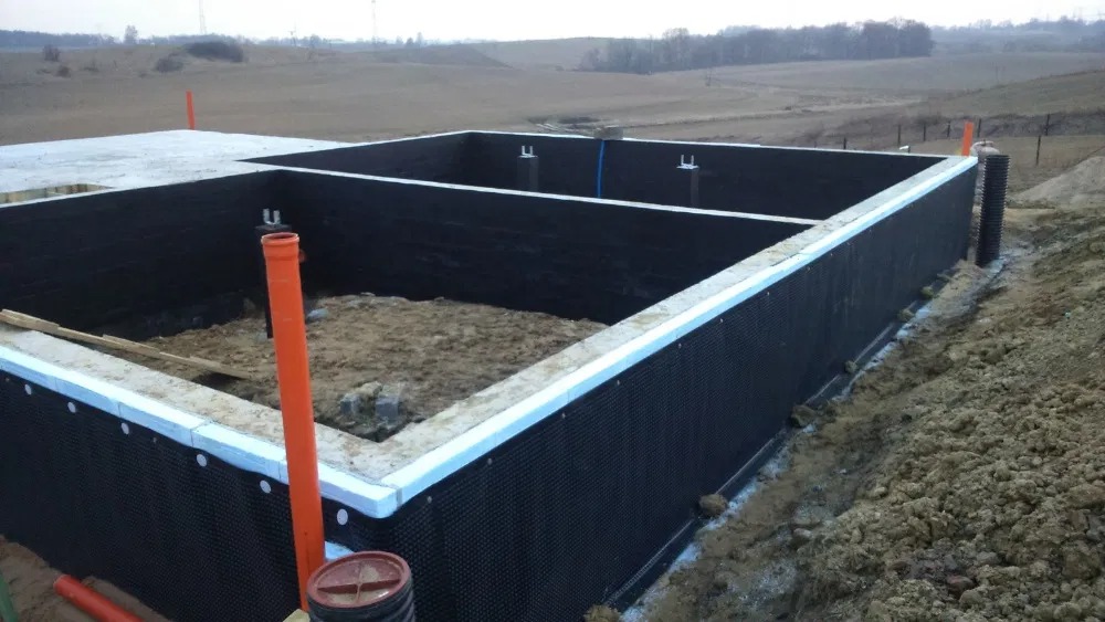 Fundament domu w trakcie budowy z hydroizolacją ścian i izolacją termiczną obrzeża.