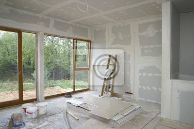 Wnętrze pokoju w trakcie remontu, ściany i sufit pokryte warstwą gładzi szpachlowej, widoczne płyty gipsowo-kartonowe, drabina oparta o ścianę, okno z widokiem na zieleń.