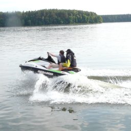 PIOTR TROJANOWSKI CRS AQUA - Dwie osoby na skuterze wodnym Sea-Doo płyną po jeziorze, za nimi widoczny las.