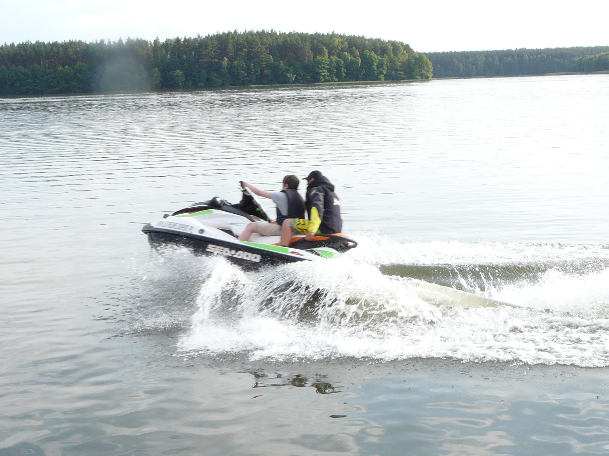 Dwie osoby na skuterze wodnym Sea-Doo płyną po jeziorze, za nimi widoczny las.