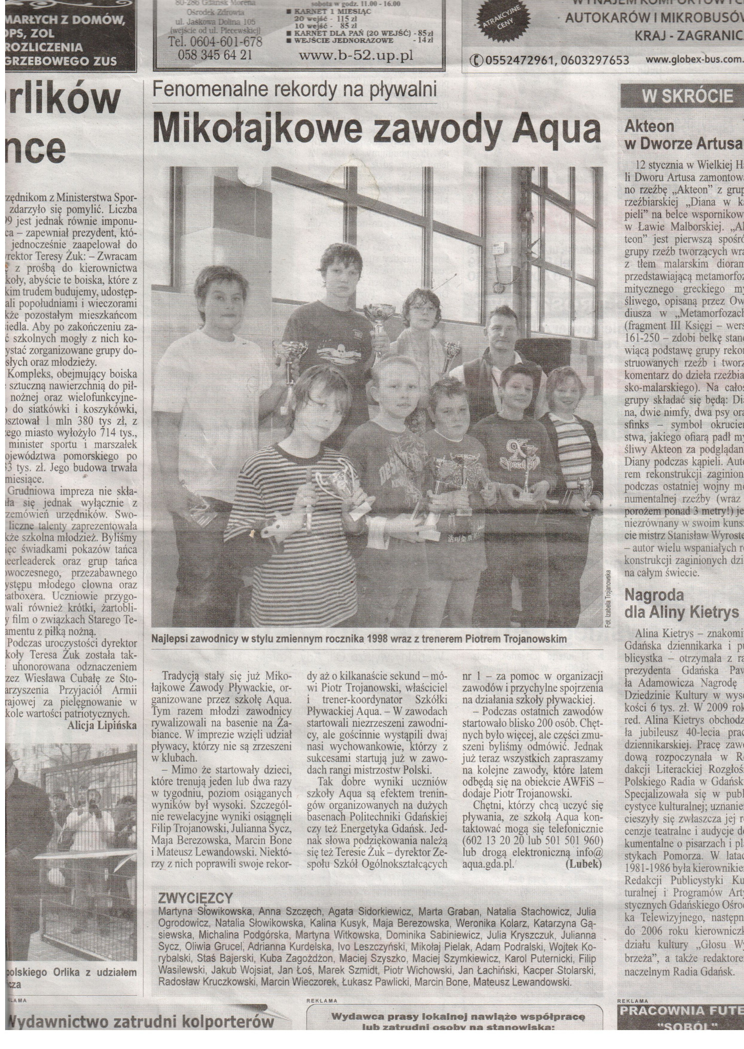 Grupa dzieci z trofeami i trenerem Piotrem Trojanowskim po Mikołajkowych Zawodach Pływackich Aqua, zdjęcie prasowe.