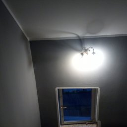 Złota rączka - Pokój po odświeżeniu: szare ściany, biały sufit, oświetlenie kinkietem i okno z widokiem na zewnątrz.