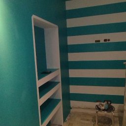 Złota rączka - Pomieszczenie po malowaniu ścian na turkusowo i białe pasy, z wnęką regałową w kolorze turkusowym, widoczne narzędzia malarskie i zabrudzenia na podłodze z parkietu.