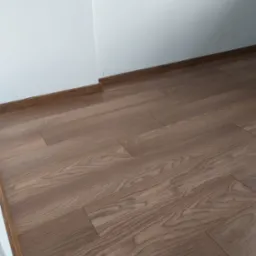 Ułożona podłoga z paneli w odcieniach brązu, widoczna przy białej ścianie z brązową listwą przypodłogową.