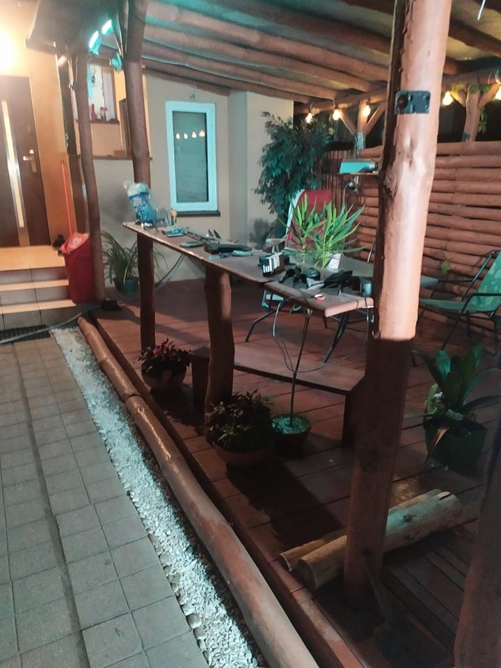 Drewniana pergola z oświetleniem w Otwocku, widok na taras z deskami, narzędzia i rośliny na stole, wieczorny nastrój.