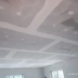 Sufit z płyt kartonowo-gipsowych w trakcie szpachlowania, widoczne łączenia płyt zabezpieczone taśmą i pokryte szpachlą, wystający kabel ze stropu.