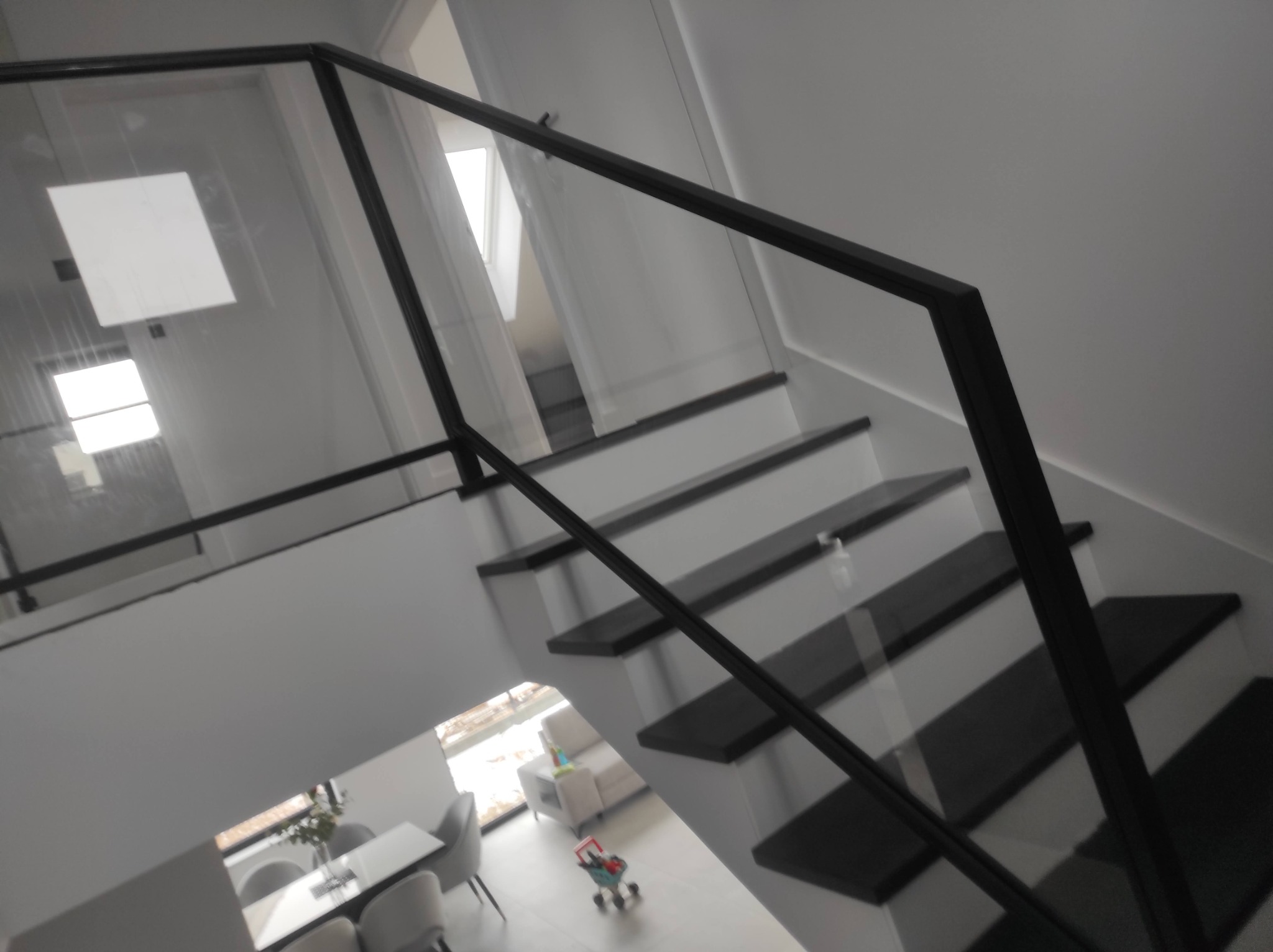 Nowoczesne schody z czarnymi stopniami i szklaną balustradą z czarną ramą, widok z góry na salon z zabawkami.
