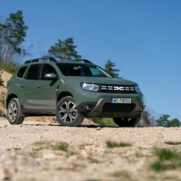 Zielony samochód terenowy marki Dacia Duster z tablicą rejestracyjną zaparkowany na piaszczystym wzgórzu w okolicy Stargardu, z widocznymi drzewami w tle pod błękitnym niebem.