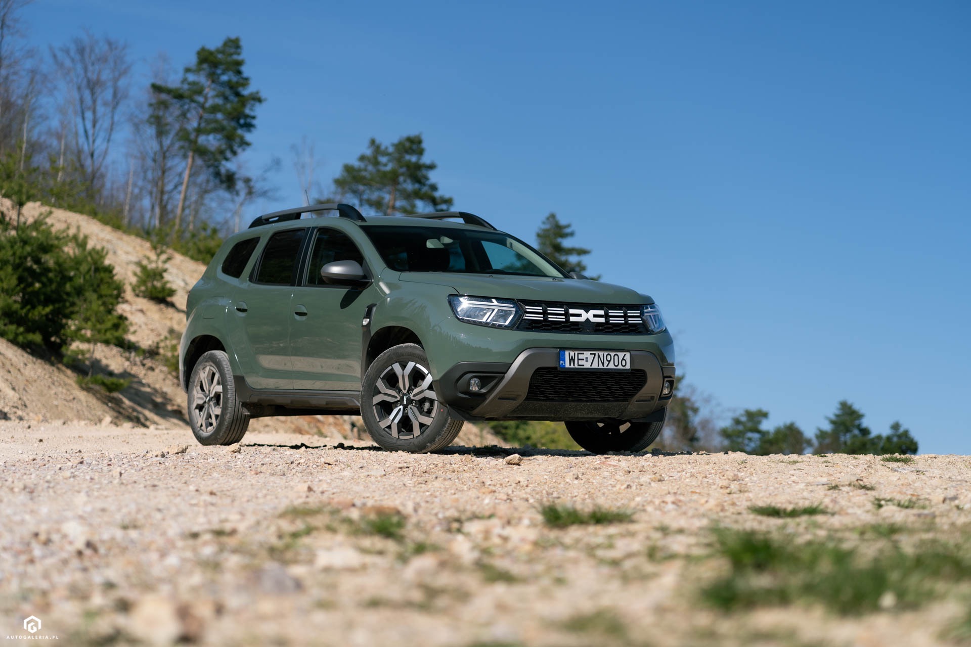 Zielony samochód terenowy marki Dacia Duster z tablicą rejestracyjną zaparkowany na piaszczystym wzgórzu w okolicy Stargardu, z widocznymi drzewami w tle pod błękitnym niebem.