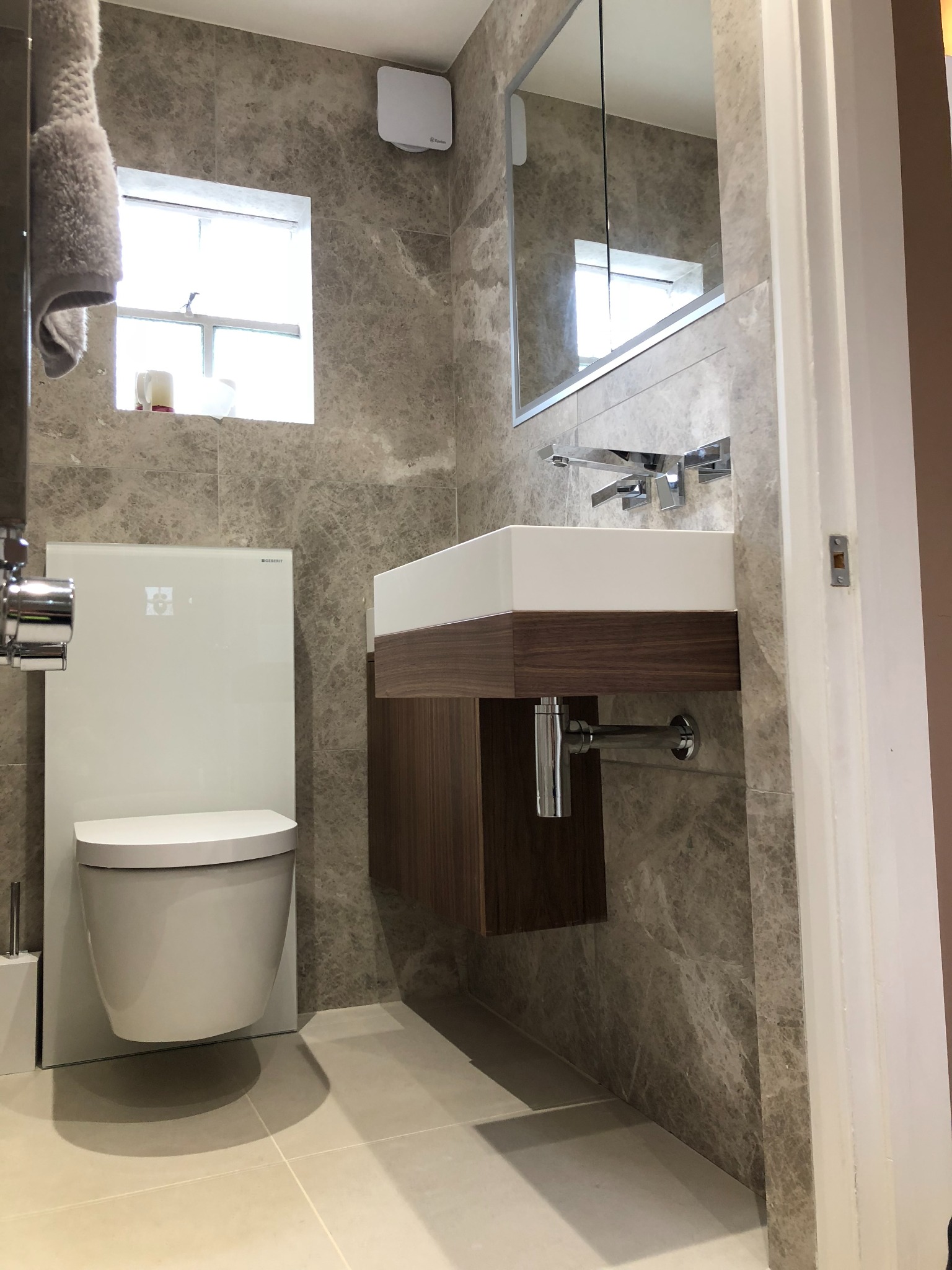Nowoczesna łazienka z marmurowymi płytkami, podwieszaną toaletą Geberit i umywalką nablatową z szafką z forniru orzechowego.