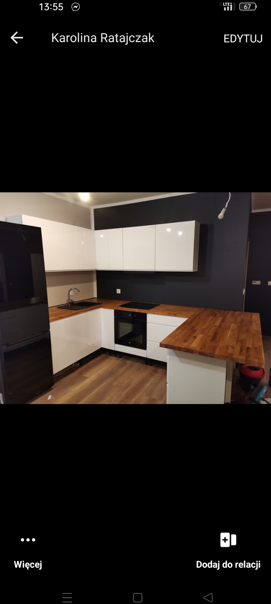 Nowoczesna kuchnia w kształcie litery U z białymi szafkami i drewnianymi blatami, ściana pomalowana na ciemny grafit, widoczny czarny zlew i sprzęt AGD.