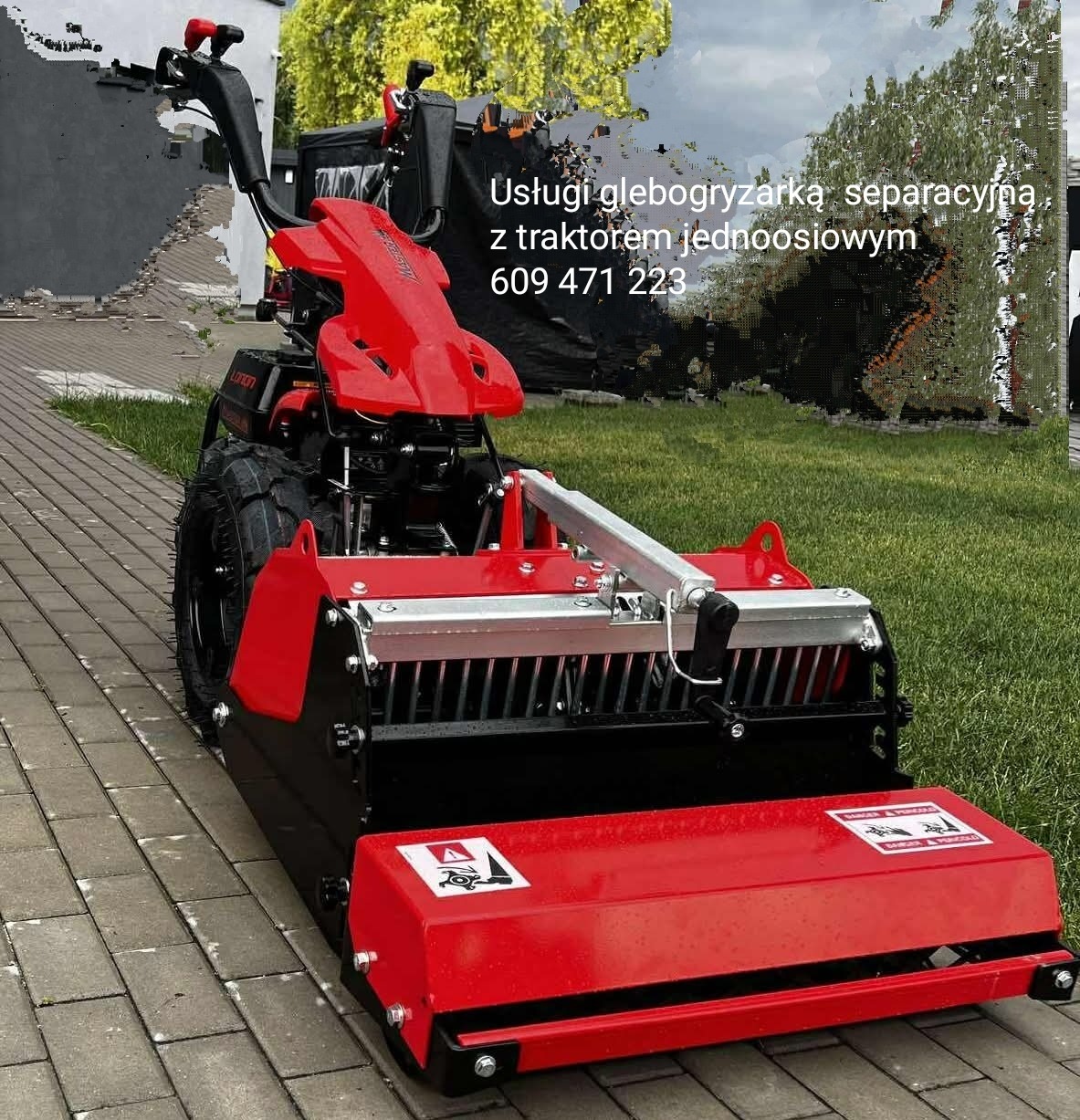 Czerwono-czarna glebogryzarka separacyjna z traktorem jednoosiowym na kostce brukowej, obok trawnika. Widoczne ostrzeżenia na maszynie.